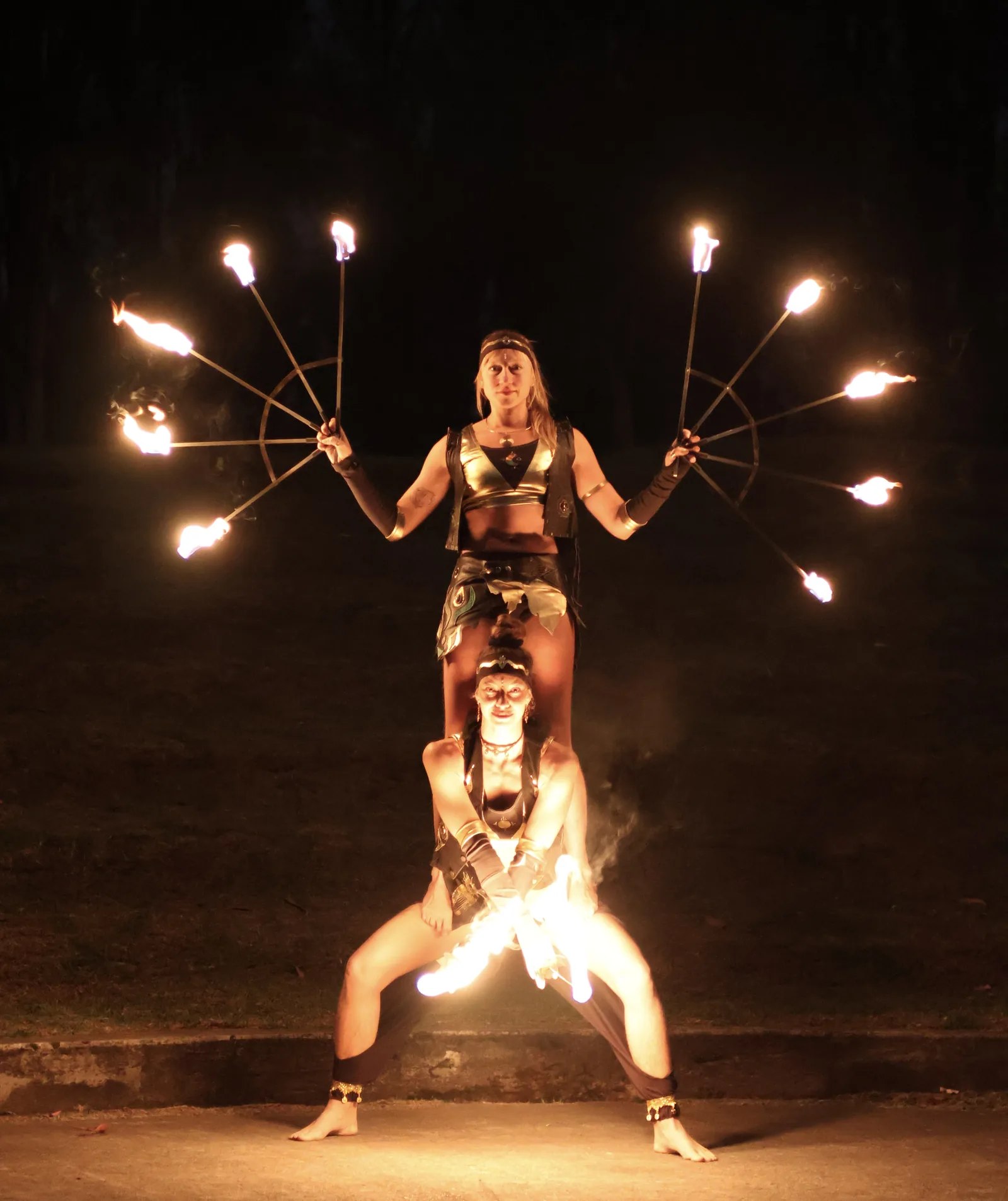 Two Kalayo performers stacked in a tower holding burning fire fans